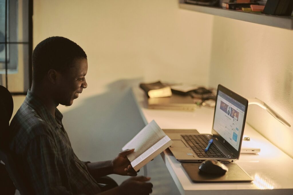 man reads a book while working at his laptop