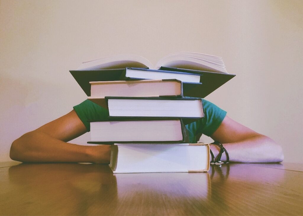 student hides head behind stack of books