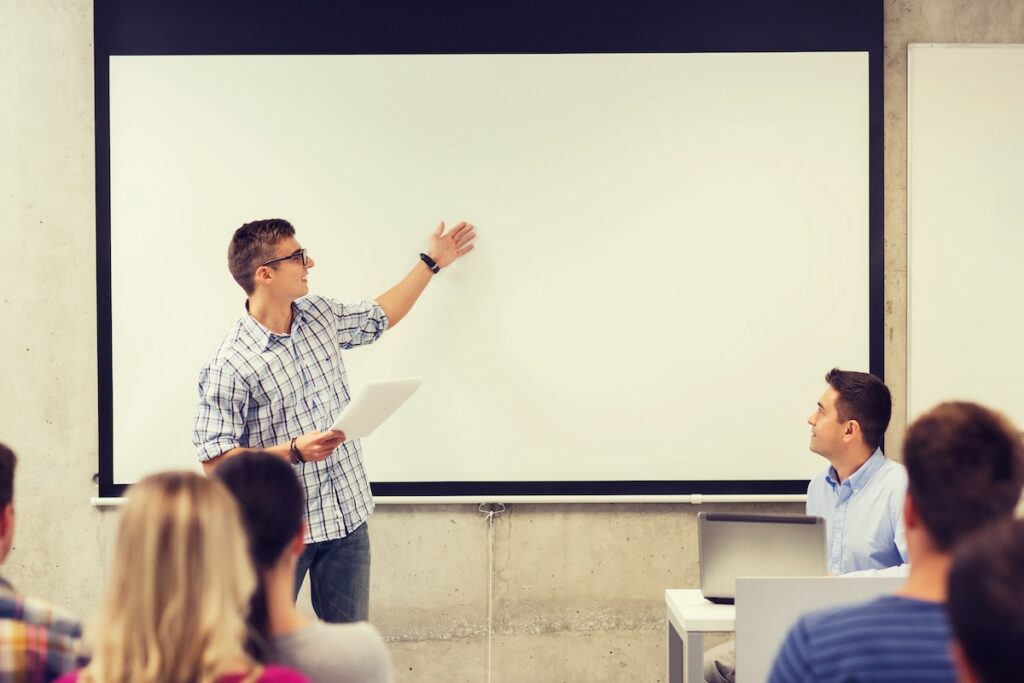 student giving speech in front of whiteboard while classmates watch