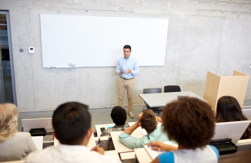 group of students and teacher with papers standing at white board at lecture