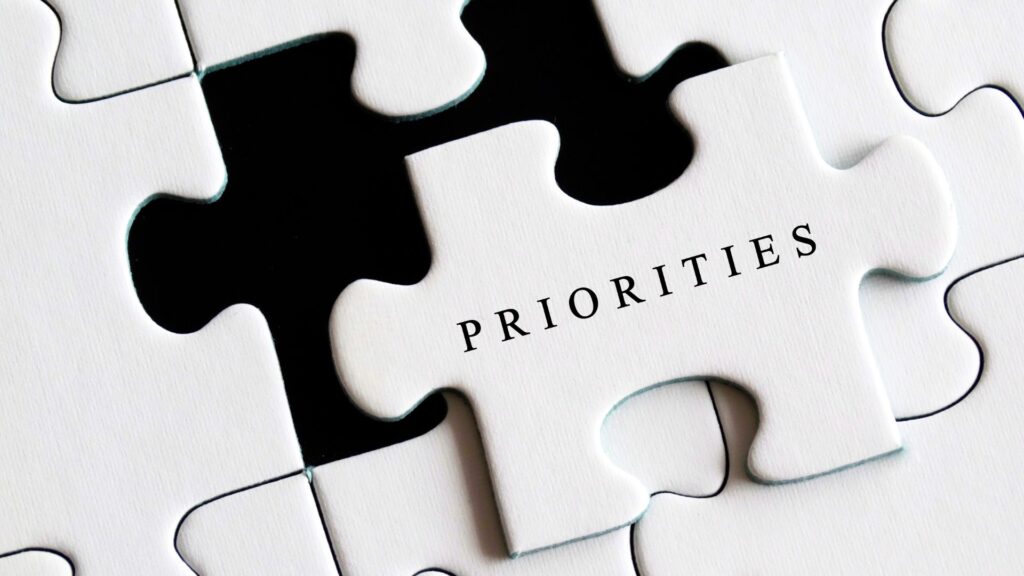 White jigsaw puzzle piece sticking out of a larger puzzle with the word "PRIORITIES" written on the piece