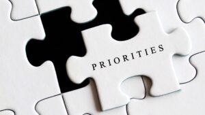 White jigsaw puzzle piece sticking out of a larger puzzle with the word "PRIORITIES" written on the piece