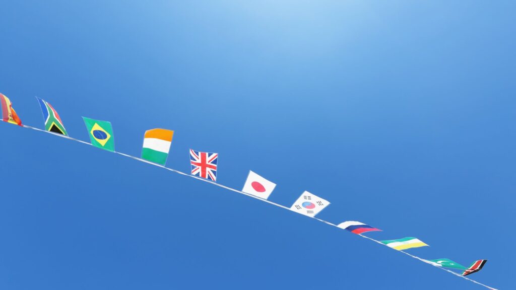 A blue sky with a string of different countries' flags, tied together on a string, waving in the wind.