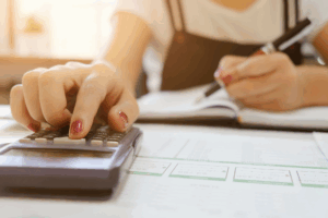 A woman enters numbers on a calculator while taking notes in a notebook