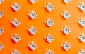 Pattern of white alarm clocks on an orange background, visually representing the time pressure and looming deadlines of early college applications.