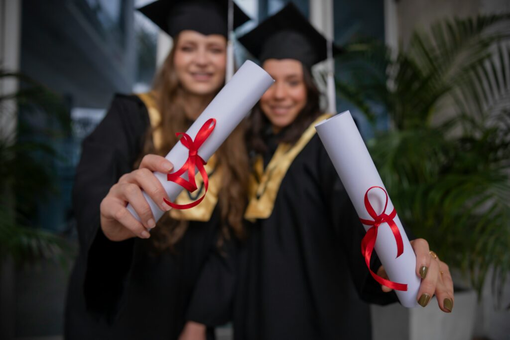 Photo of two high school graduates holding their diplomas with red ribbons on graduation day