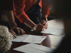 Hands writing a letter of recommendation for graduate school at a desk of documents