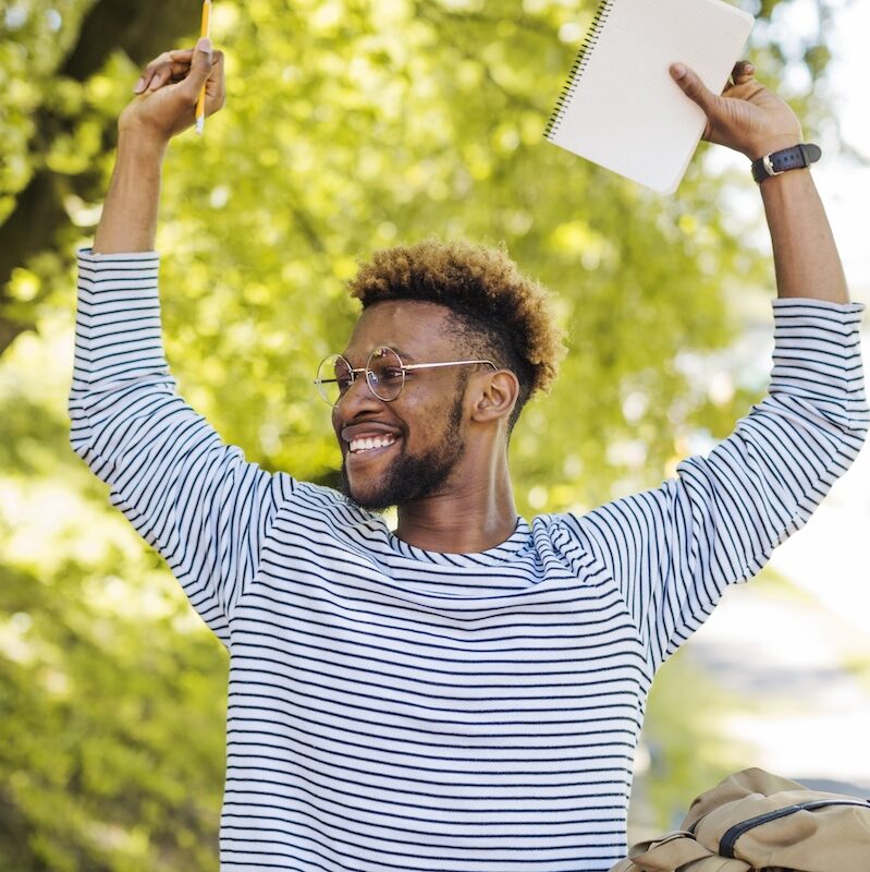 excited student smiles with hands raised over his head